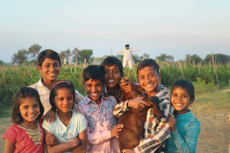 Group of young Indian children smiling holding a goat  in the country side.