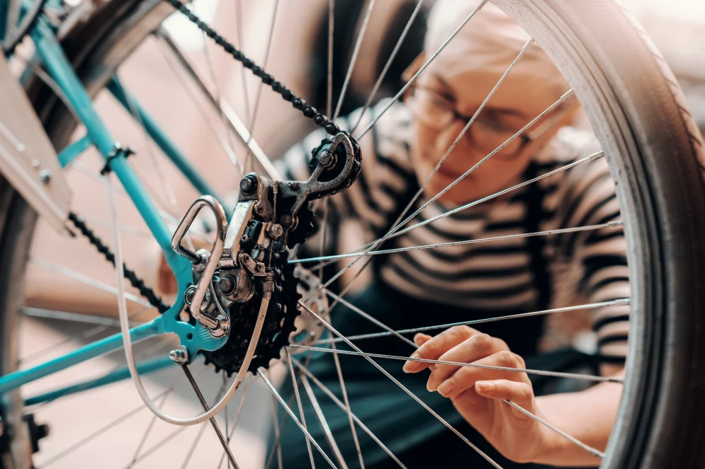 A women is focused on repairing the rear gear of a turquoise bicycle.