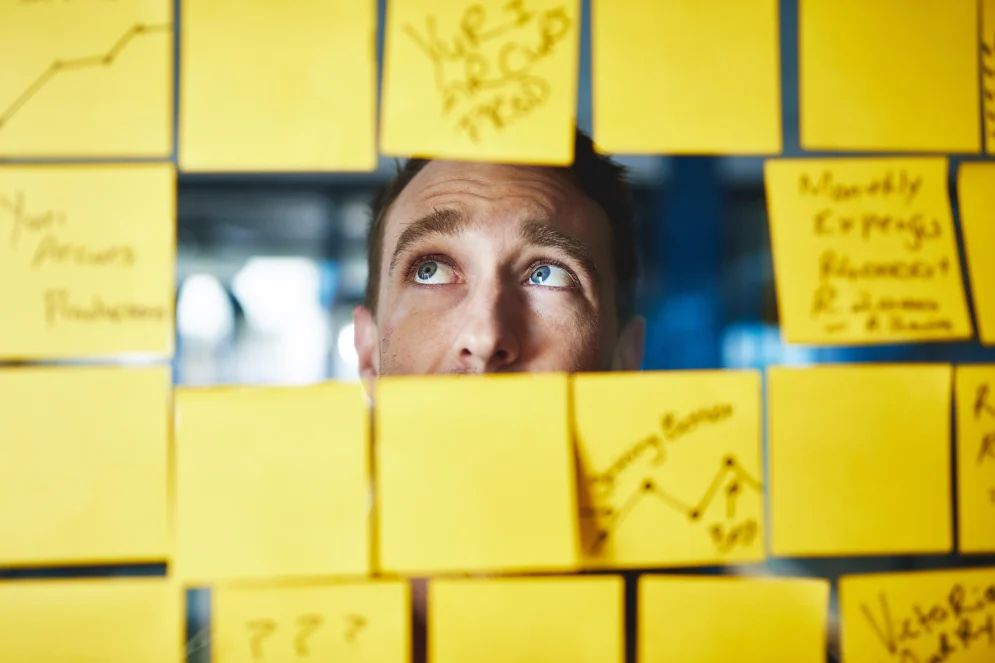 A person looking anxiously out through a wall of yellow sticky notes.
