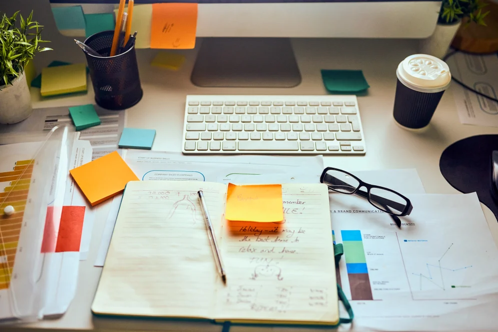 A cultured desk in front of a computer and keyboard with documents and a note book open ready for review.